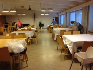 Meilahden kirkon seurakuntasali, jonka pöydille asetellaan valkoisia liinoja.